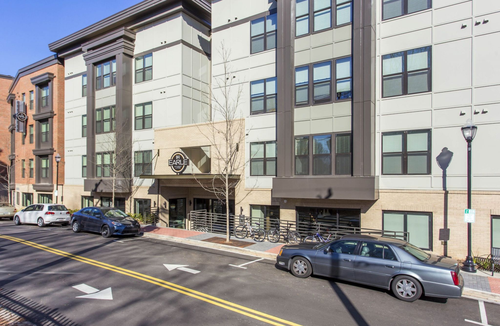 Modern apartment building at 114 Earle features large windows, multiple floors, and cars parked along the street in front.