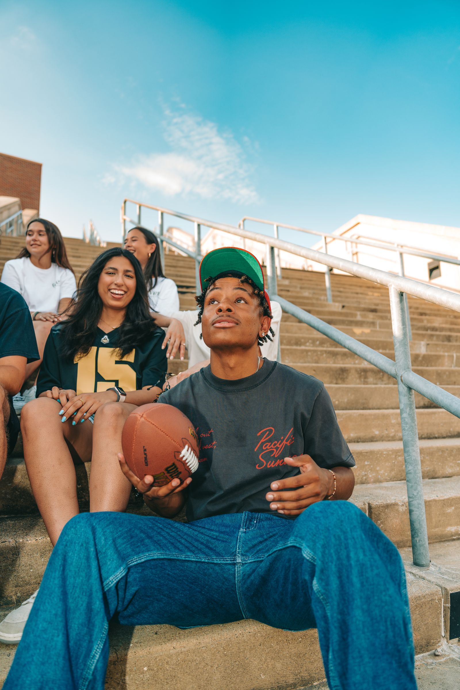 A group of friends sitting on outdoor steps, with one person holding a football and looking up.