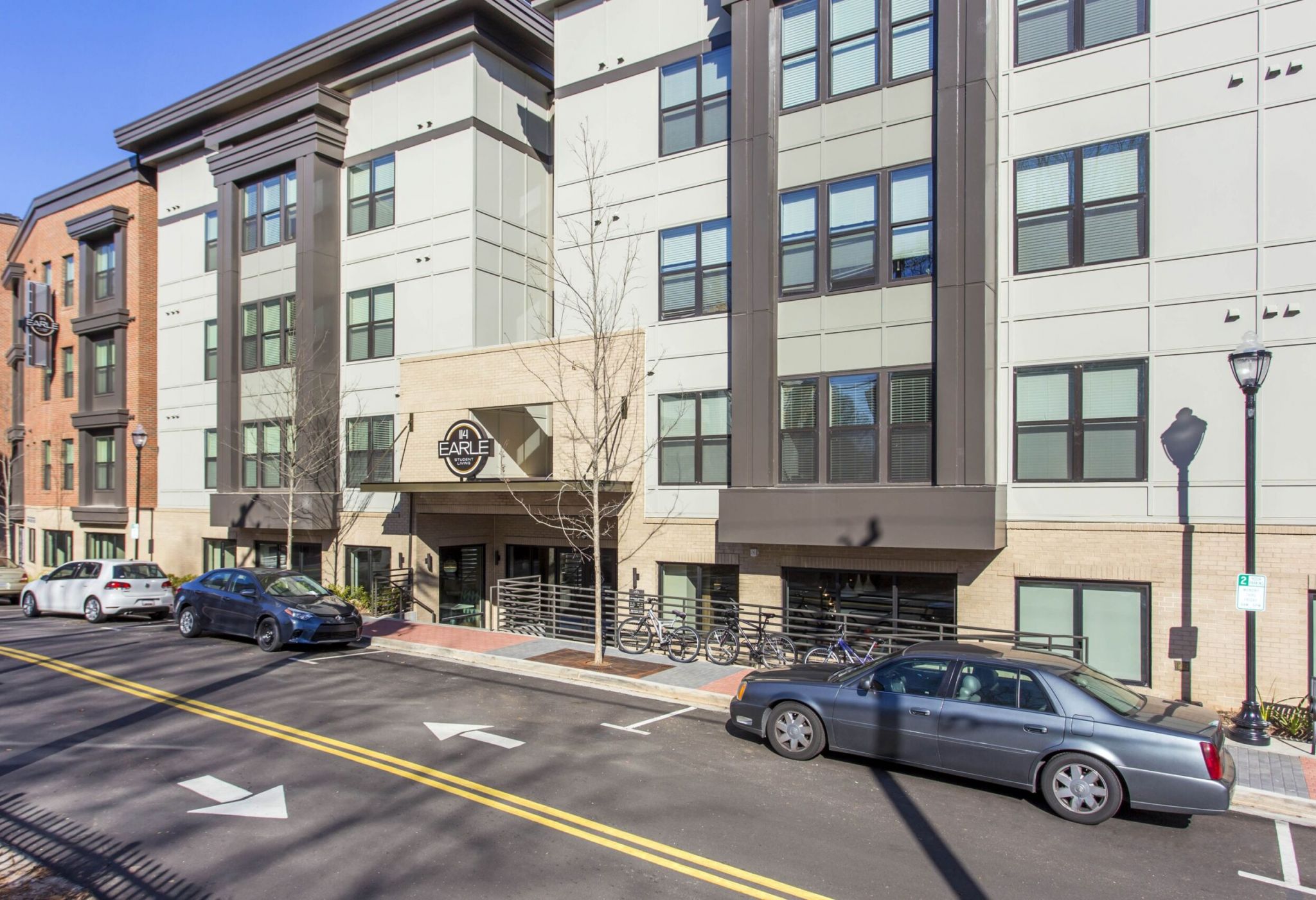 Modern apartment building at 114 Earle features large windows, multiple floors, and cars parked along the street in front.