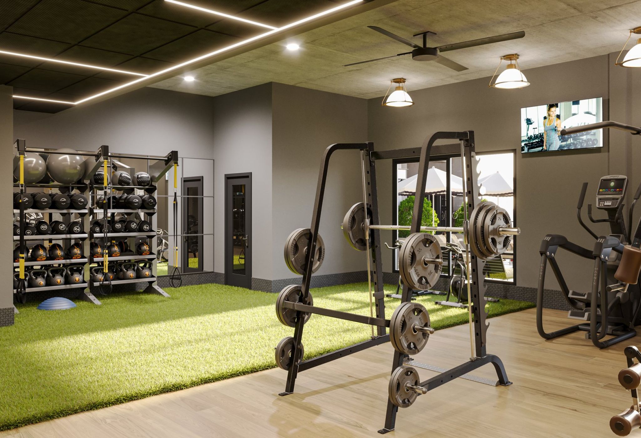 A modern gym in LOCAL Nashville with weight racks, exercise balls, and various fitness equipment, including treadmills and weightlifting machines, on hardwood and artificial grass flooring. The room is well-lit with ceiling lights and windows, featuring a wall-mounted TV.