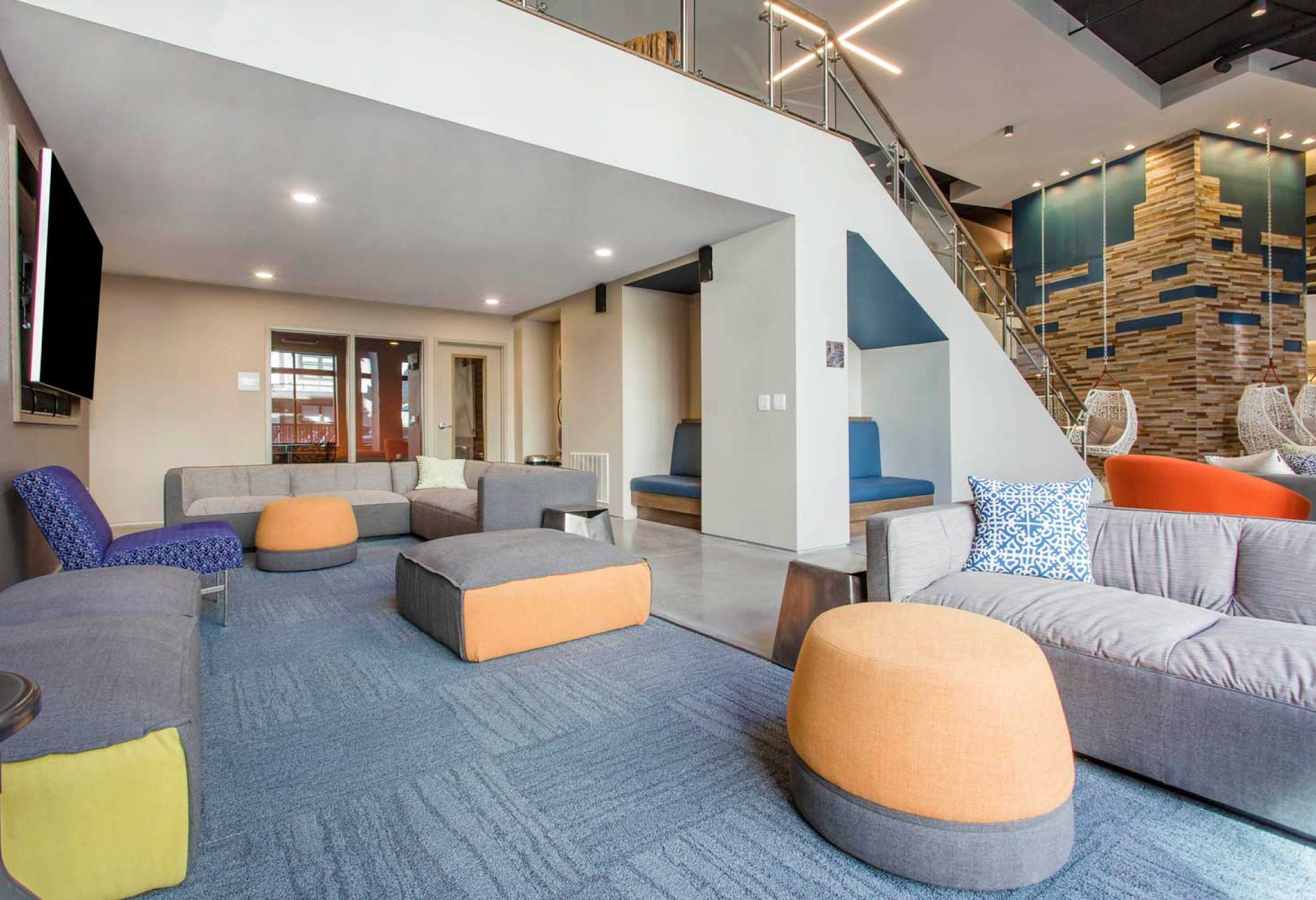 Modern lounge area at 114 Earle features sofas, colorful chairs, and a staircase leading to a mezzanine level with more seating.