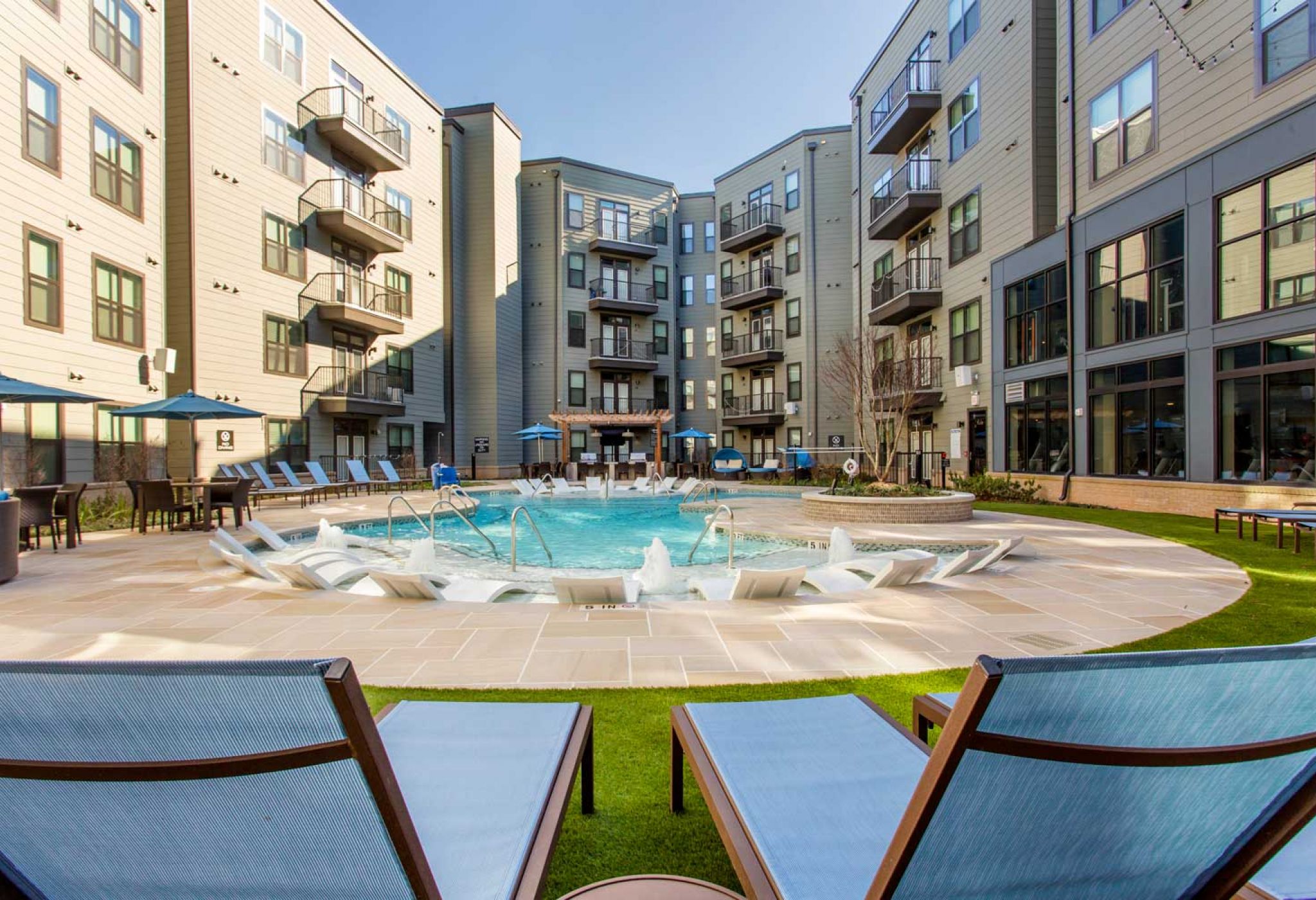 Modern apartment complex at 114 Earle with a central circular outdoor pool, lounge chairs, and surrounding multi-story buildings.