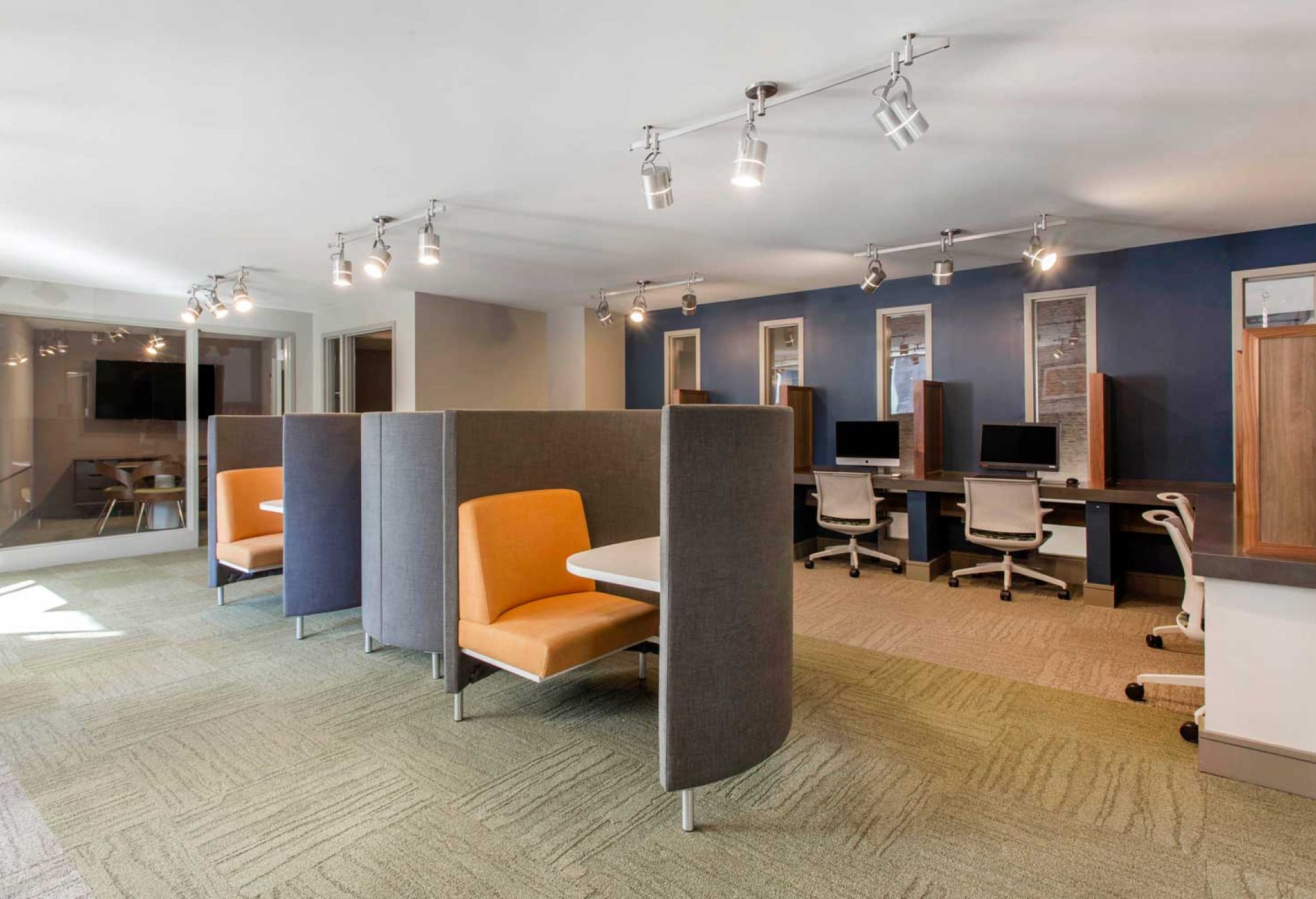 Located at 114 Earle, this modern office space boasts individual workstations, state-of-the-art computers, and divided seating areas featuring orange cushioned chairs.