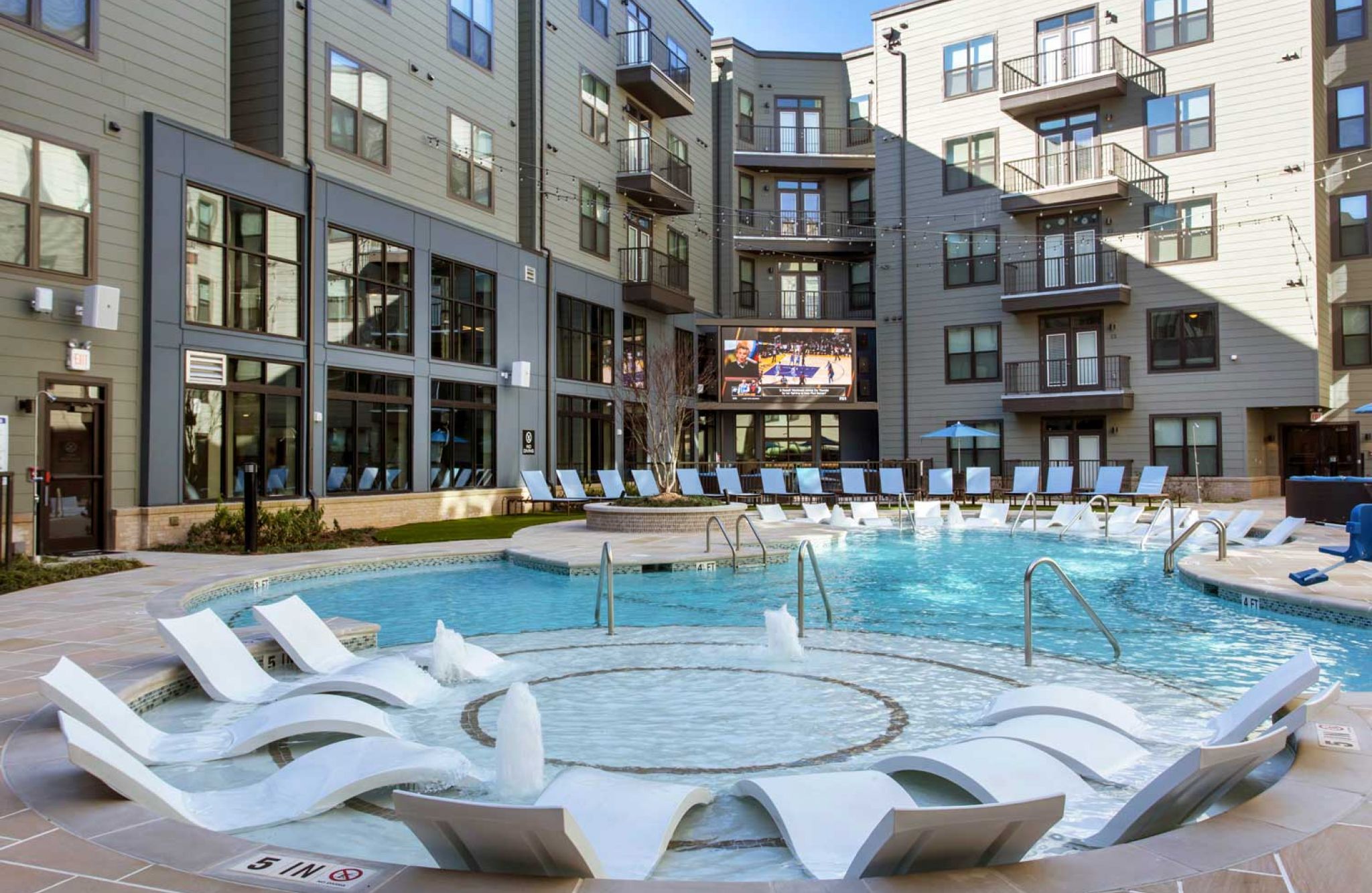 Modern apartment complex 114 Earle features a luxurious pool area, lounge chairs, and an outdoor TV screen.