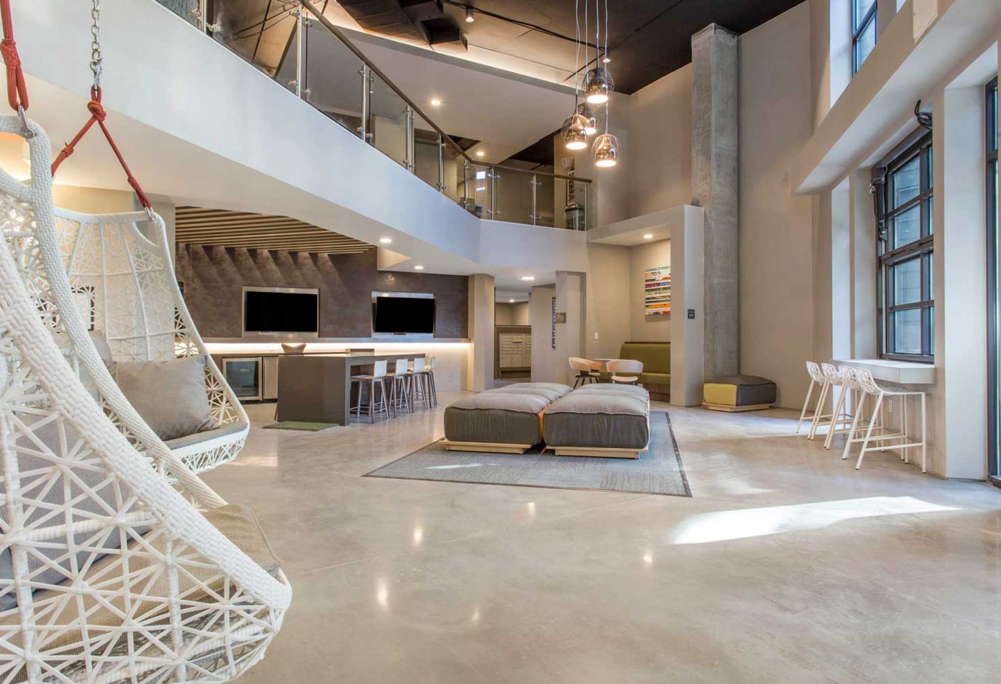 Modern and spacious living area at 114 Earle, featuring hanging chairs, cozy seating, a kitchen, and large windows.