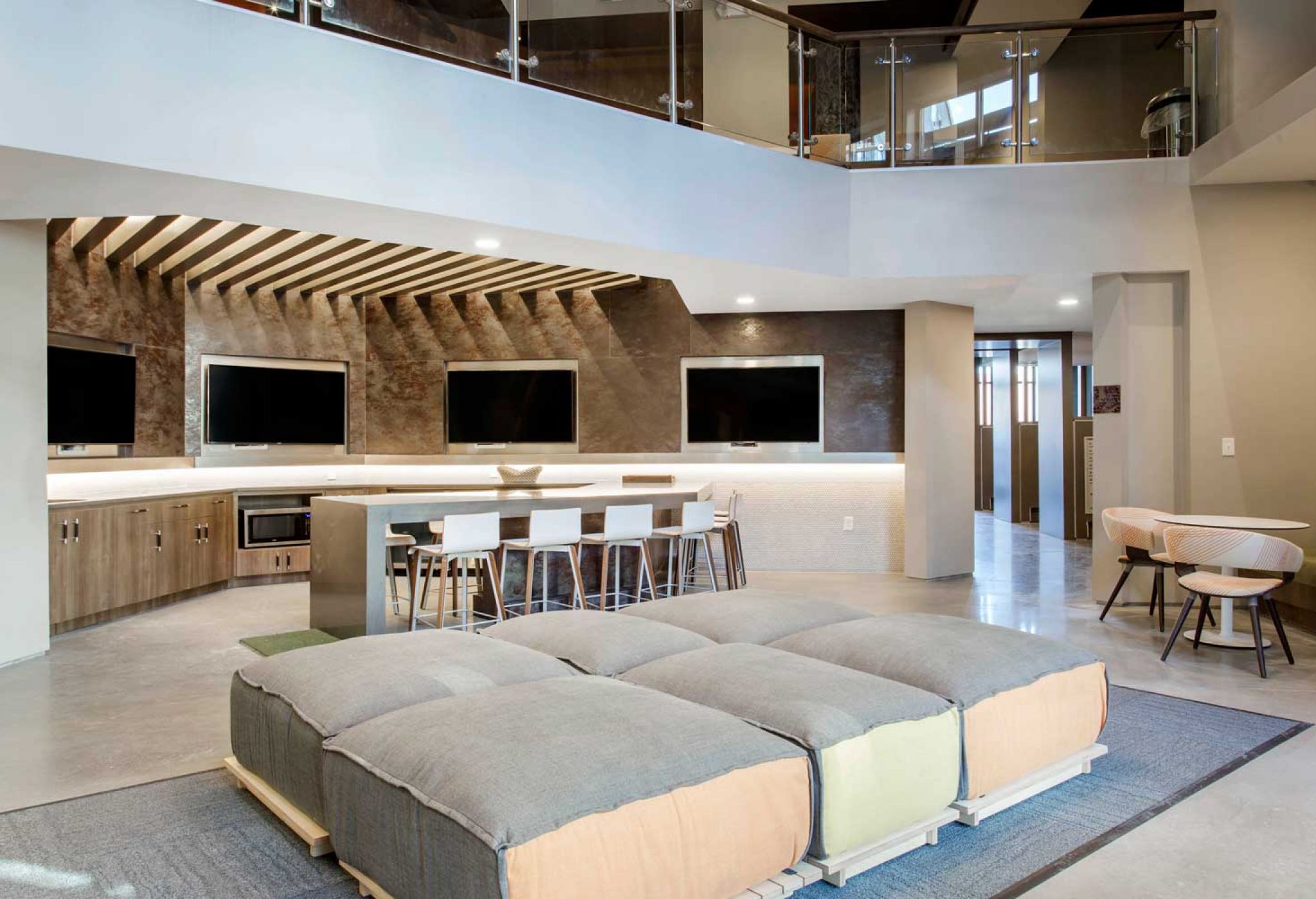 A modern lounge at 114 Earle features cushioned seating, bar stools at a counter, and four mounted TV screens under a slatted wooden ceiling.