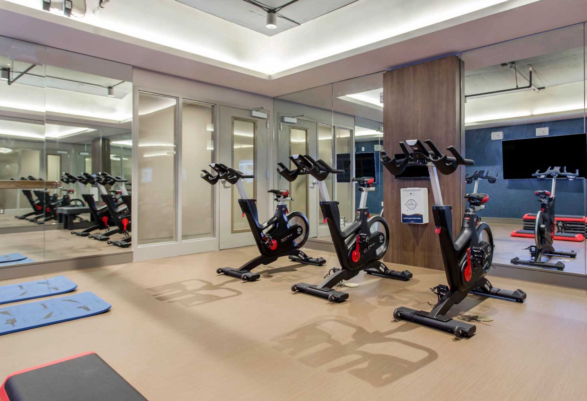 114 Earle offers luxury living with a modern gym interior featuring stationary bikes, exercise mats, mirrors, and a wall-mounted TV.