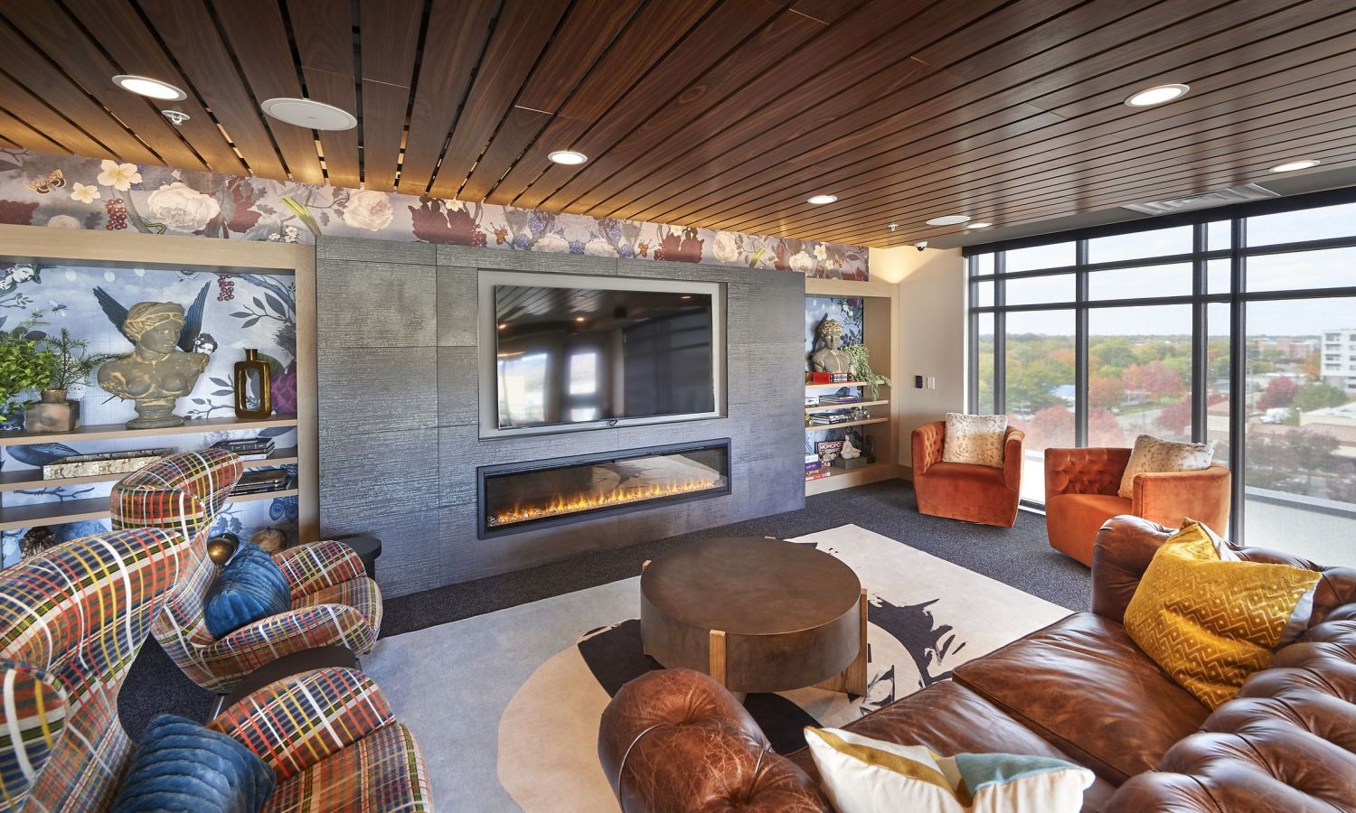 Cozy living room with cushioned chairs, modern fireplace, plaid and leather seating, and large windows offering a scenic Boise view.