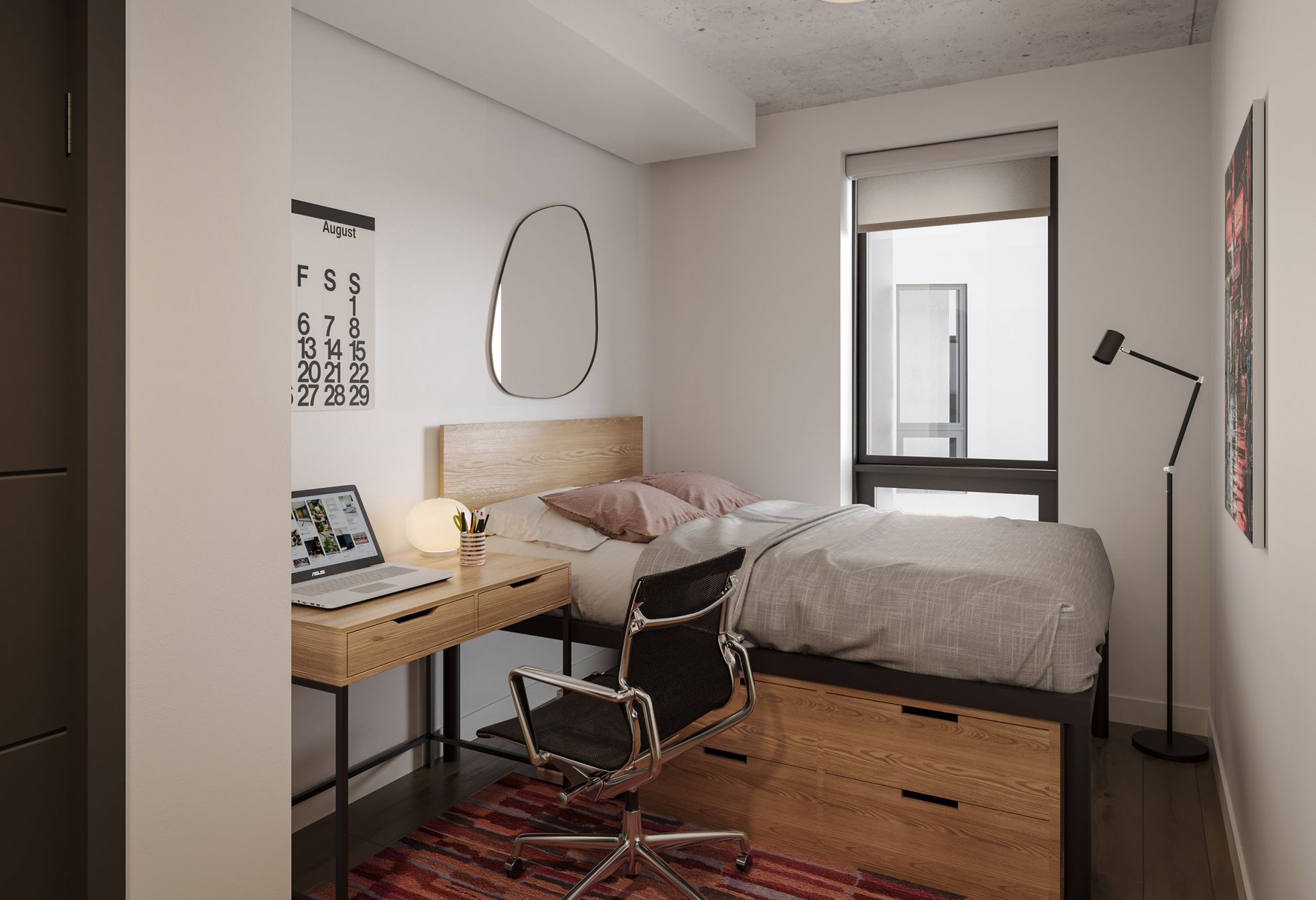 A neatly organized VERVE Madison bedroom features a bed with light gray bedding and two pillows, next to a wall-mounted mirror. A wooden desk with a laptop, lamp, and chair is beside the bed. A calendar hangs on the wall, and a floor lamp stands near a window with blinds.