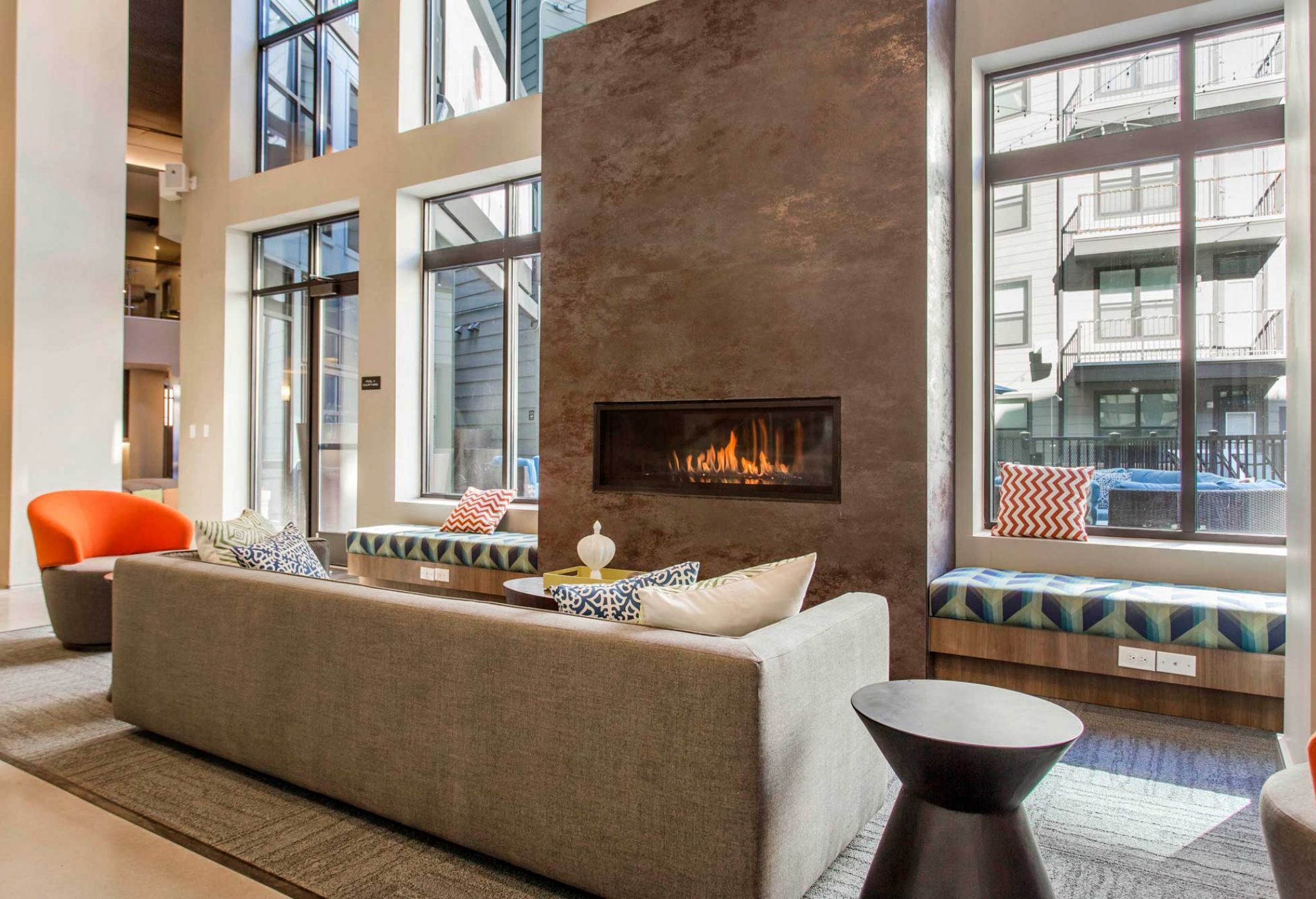 Modern living room at 114 Earle with a large fireplace, grey sofa, orange chairs, and tall windows offering a charming street view.