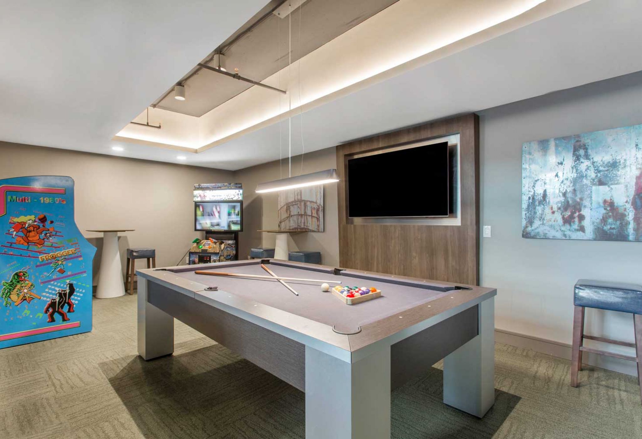 Recreation room at 114 Earle with a pool table, arcade machine, two bar stools, a large TV, and framed artwork on the wall.