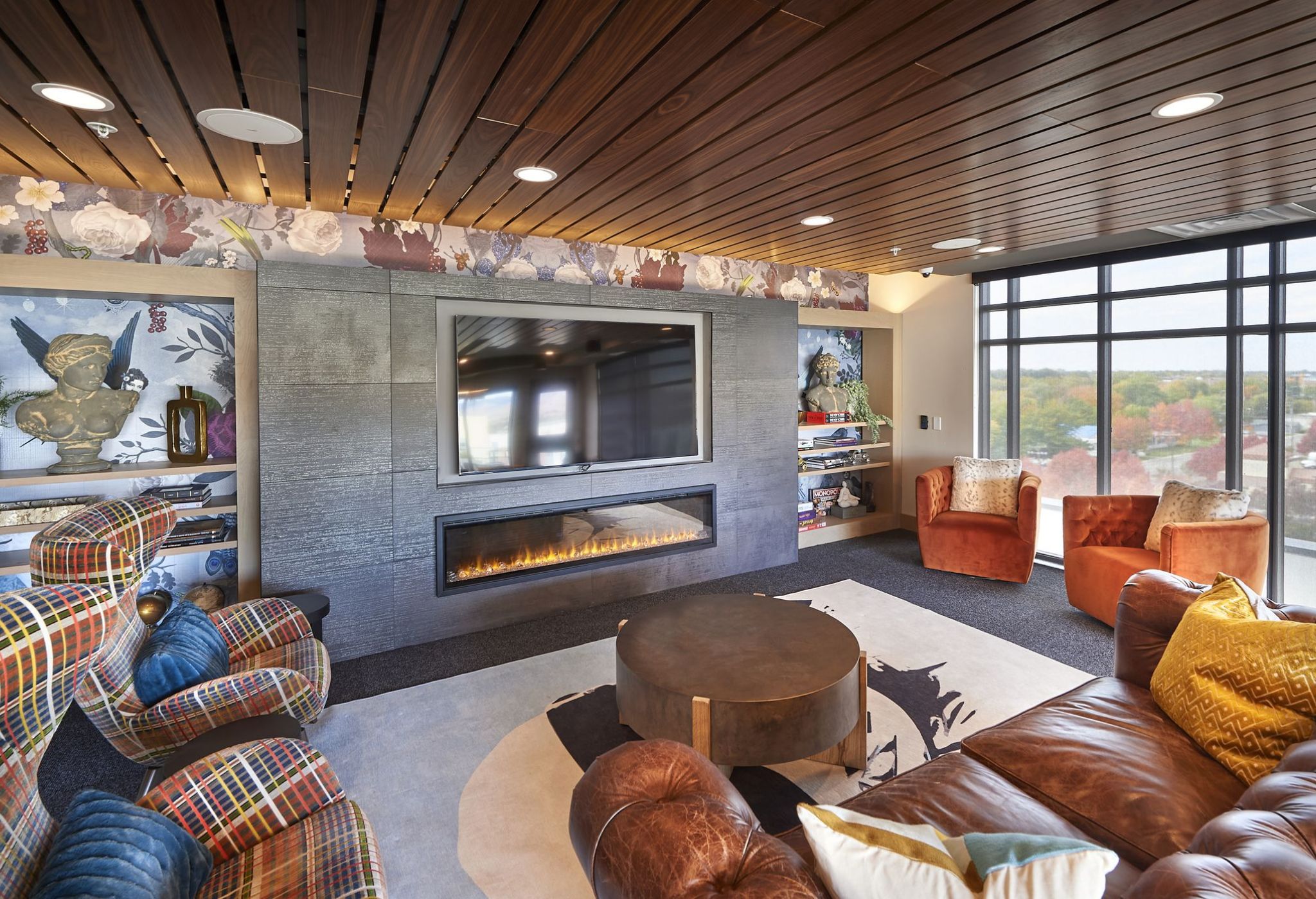 Cozy living room with cushioned chairs, modern fireplace, plaid and leather seating, and large windows offering a scenic Boise view.