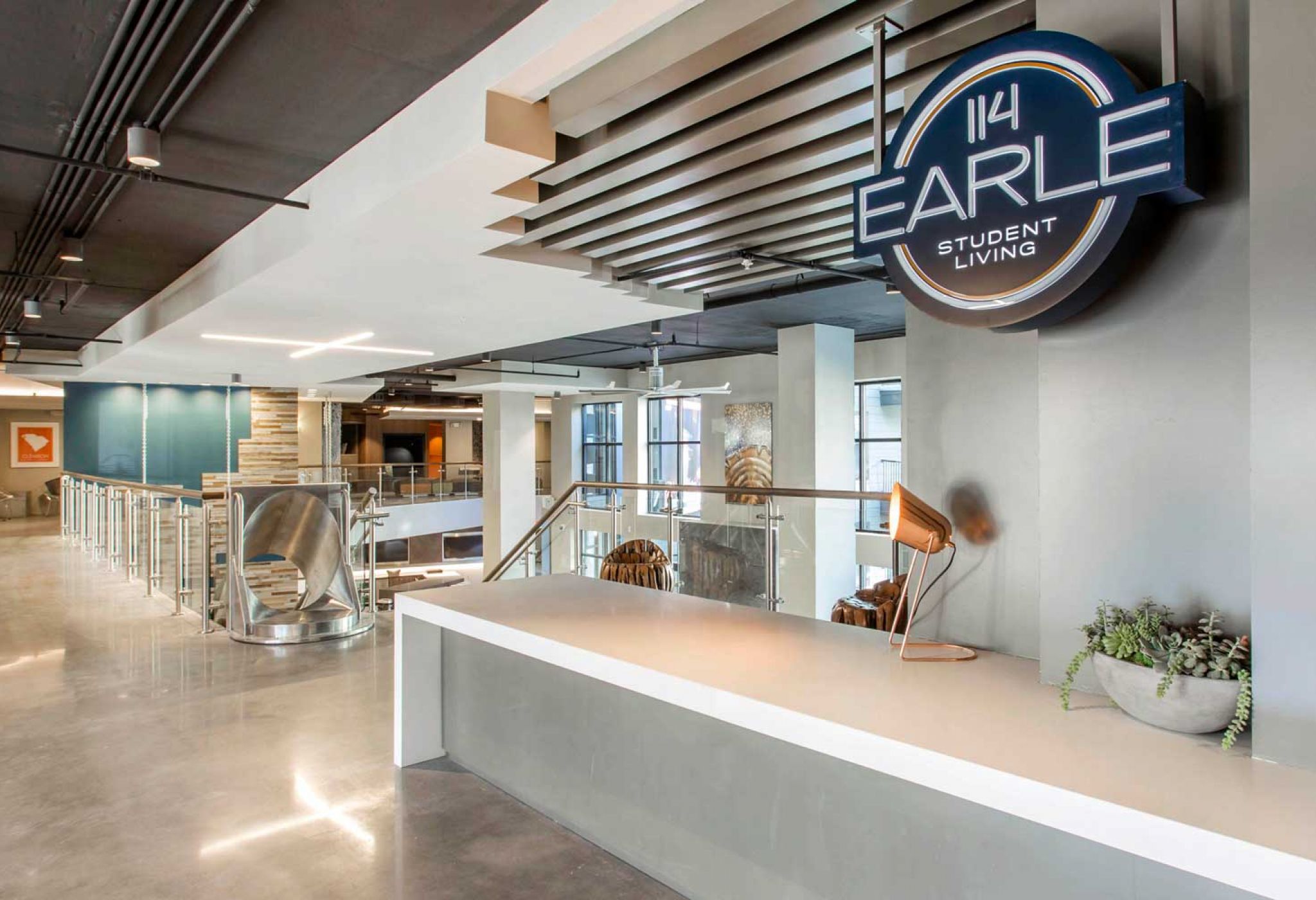 Modern interior view of 114 Earle Student Living with a sign, sleek counter, and a spiral slide in the background.